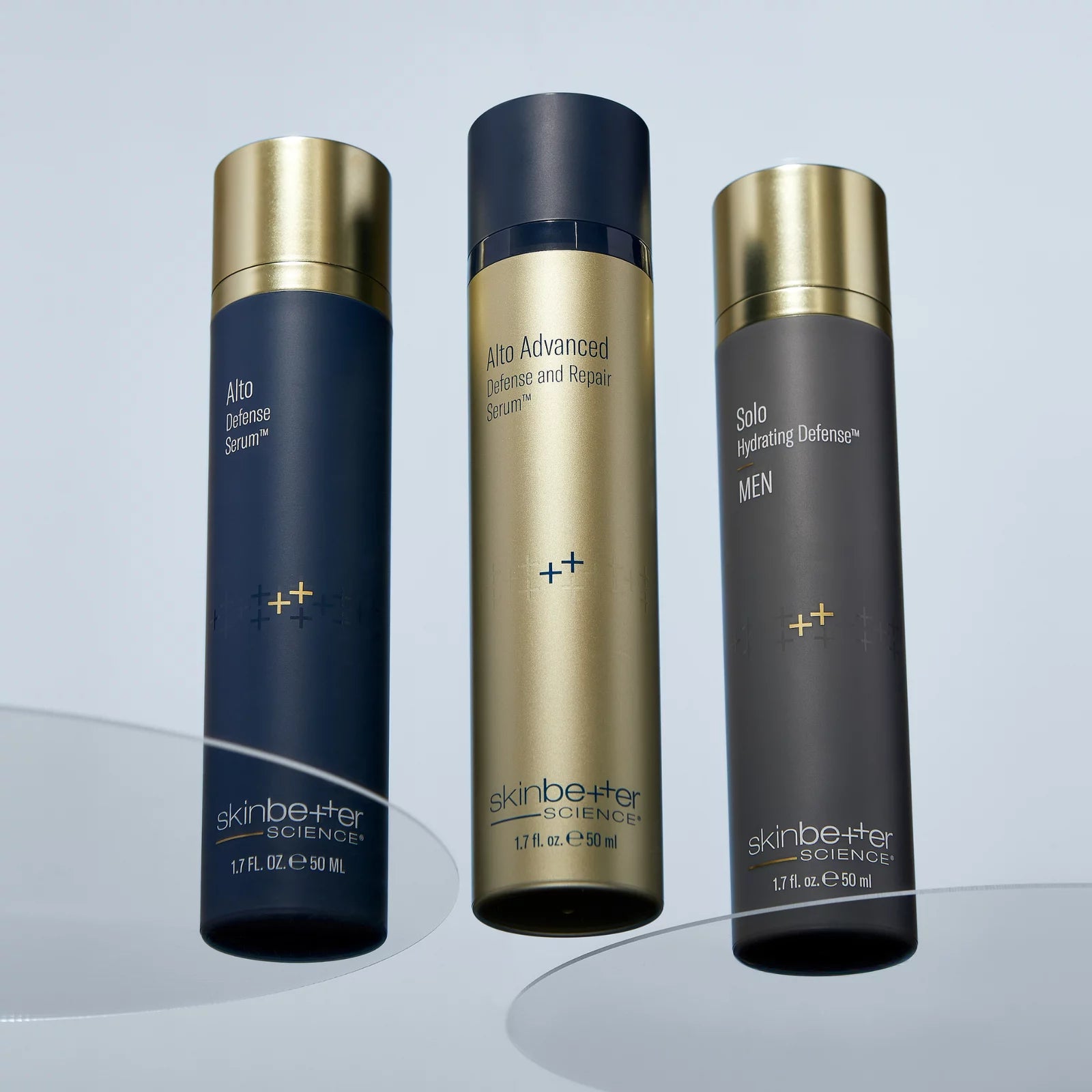 Three skincare bottles from skinbetter SCIENCE on a light gray studio background. The left bottle is dark navy blue with a gold cap, labeled Ally Hyaluence Serum.
